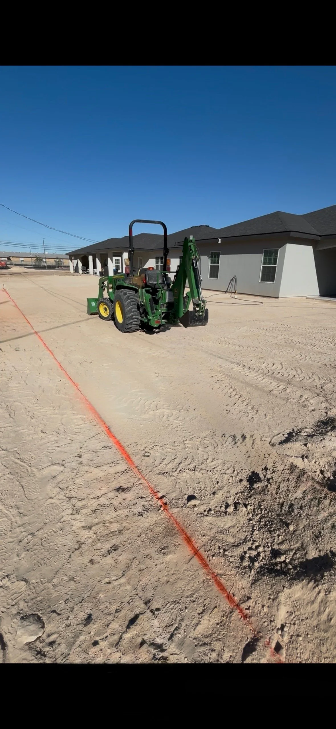 Construction site with a green tractor and an orange marking line on the ground in front of a house.