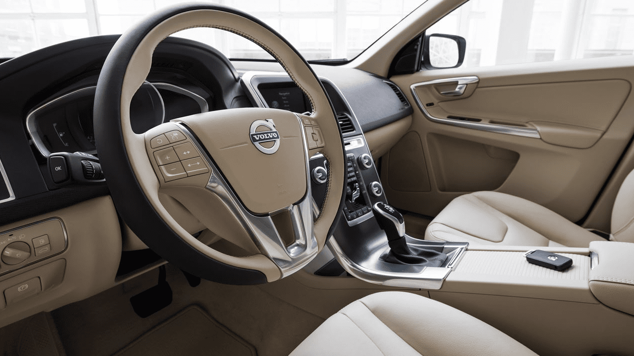 Interior of a clean beige car showing steering wheel, dashboard, gear shifter, and front seats.