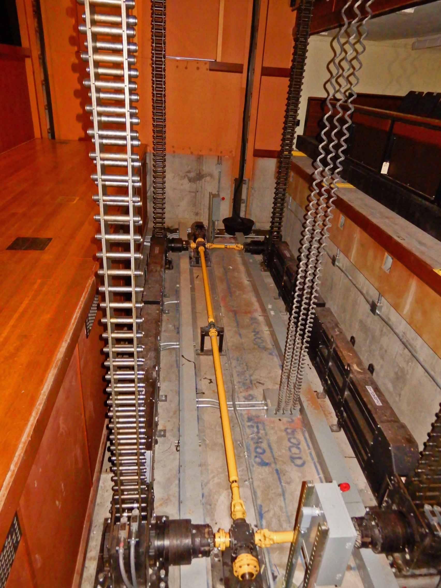Stage lift motor and electrical equipment, including yellow pipes, black machinery, and metal chains.