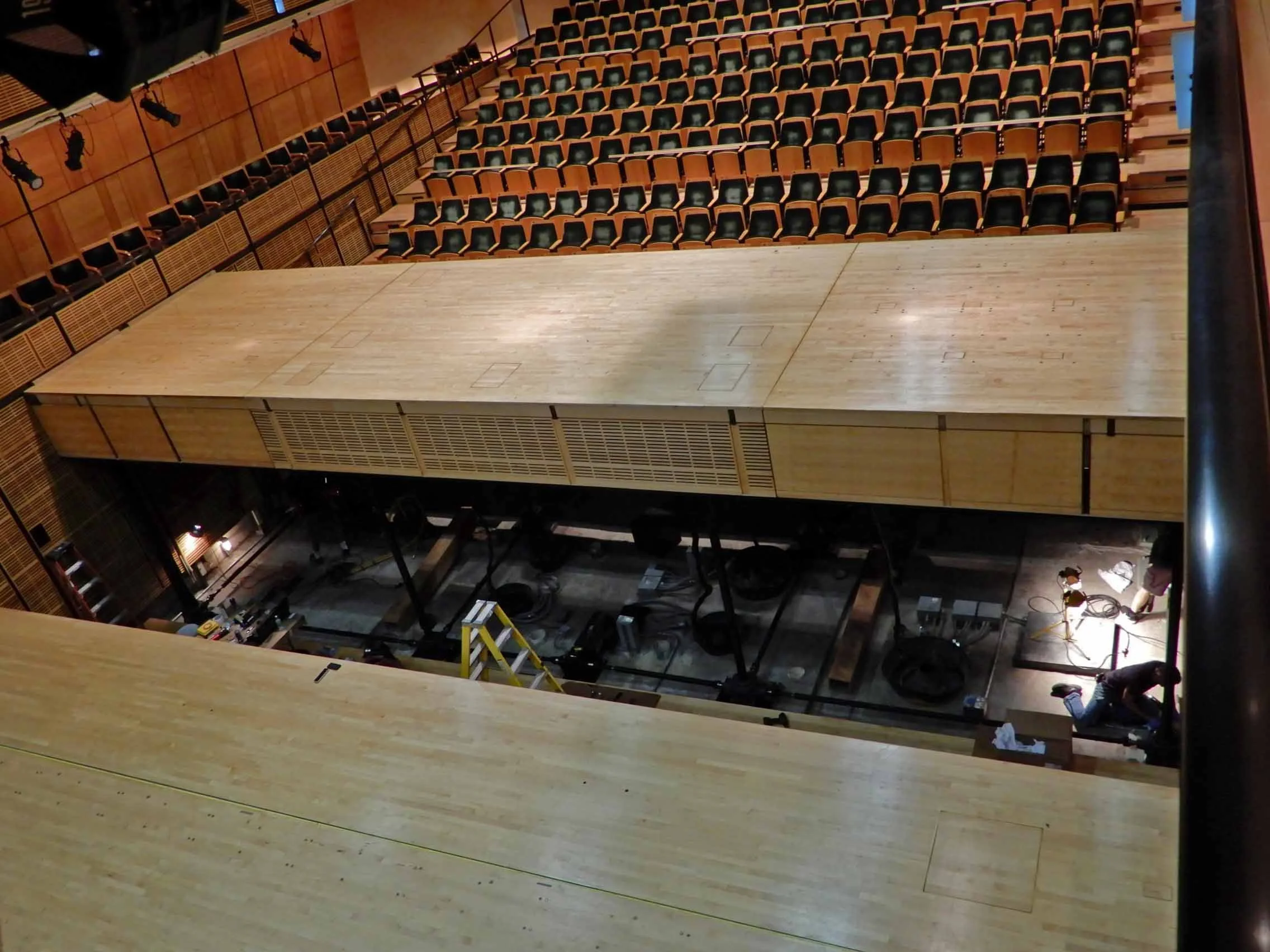 Picture of work being done on a pit orchestra, with the pit open, tools and a ladder.