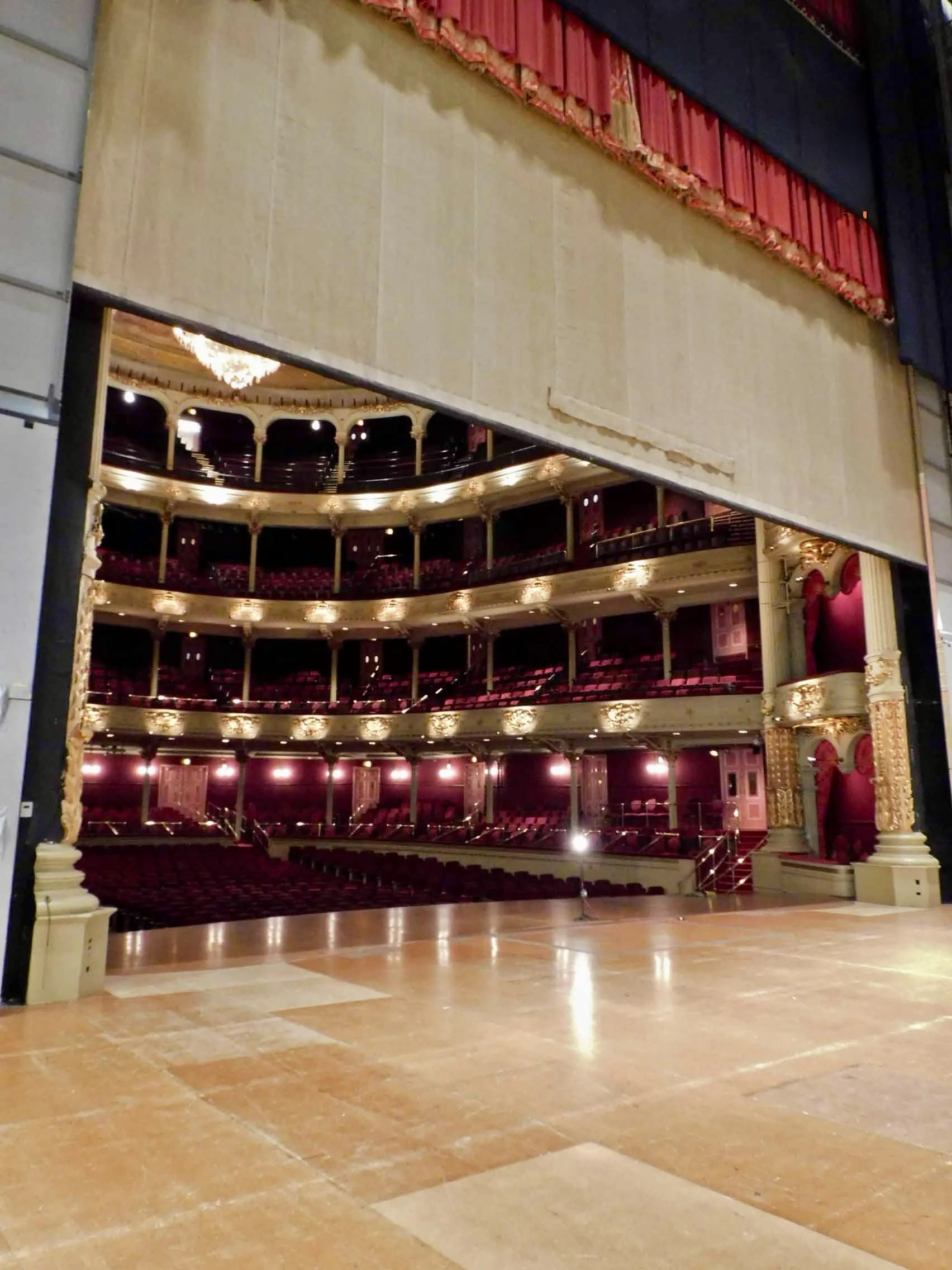 Large theater, from backstage to house, with fire curtain halfway closed.