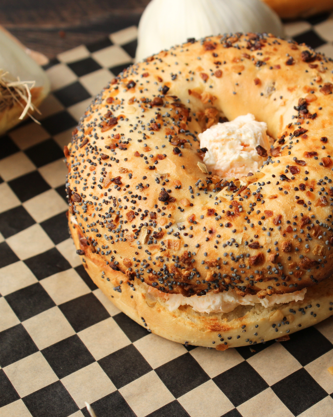 Sesame seed bagel with cream cheese on a checkered surface.