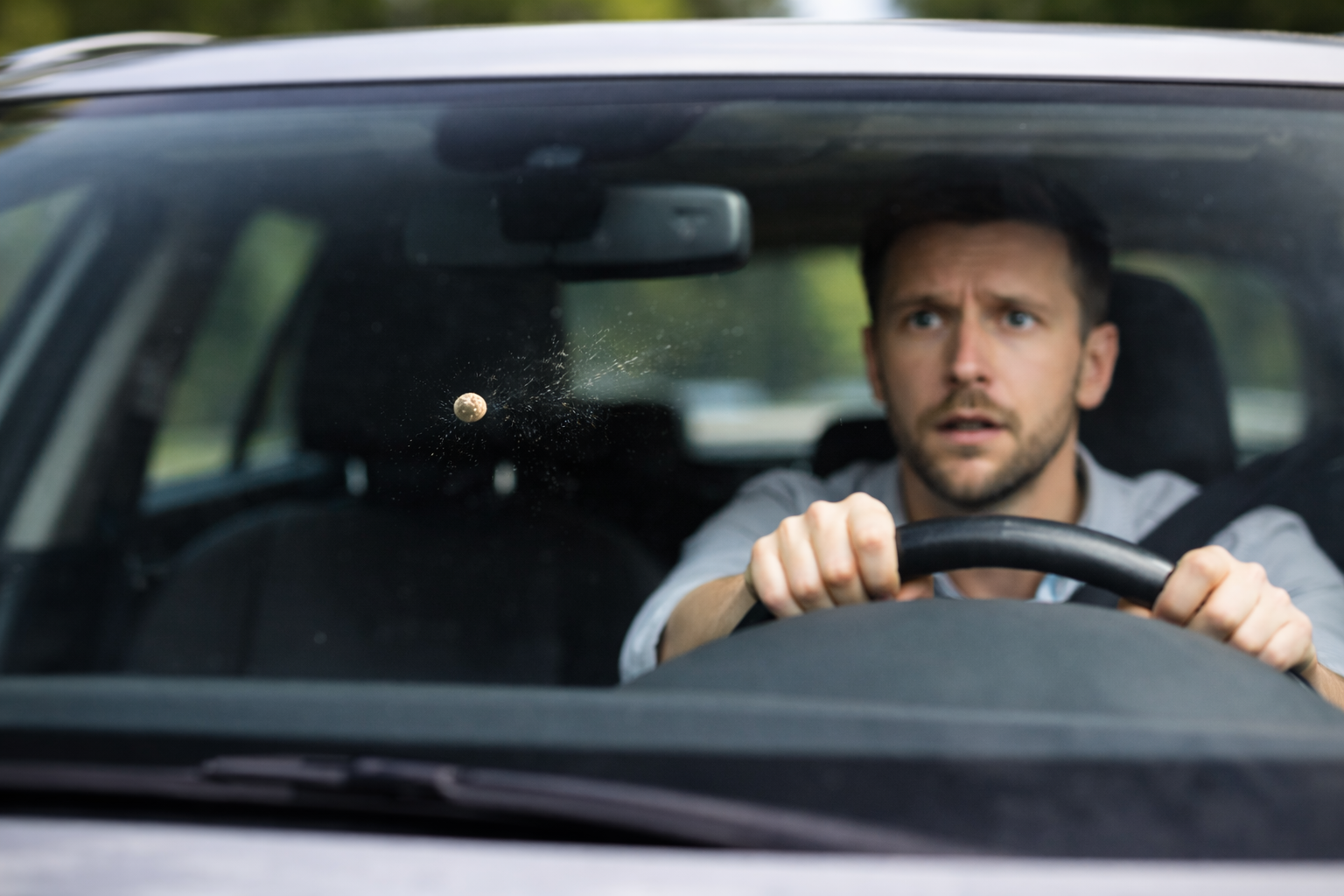 A man driving a car with a cricket ball hitting the windshield.