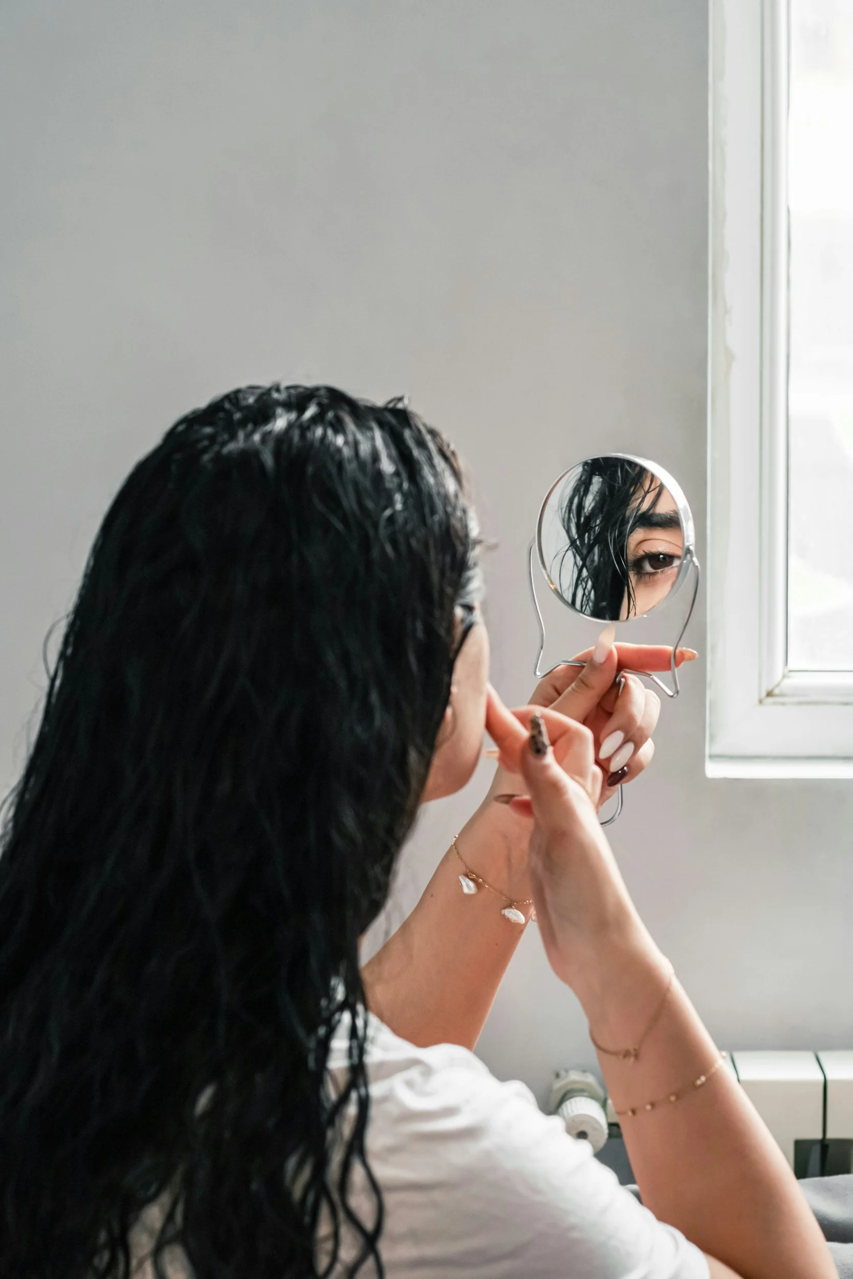 Woman applying eye makeup while examining her reflection in a handheld mirror