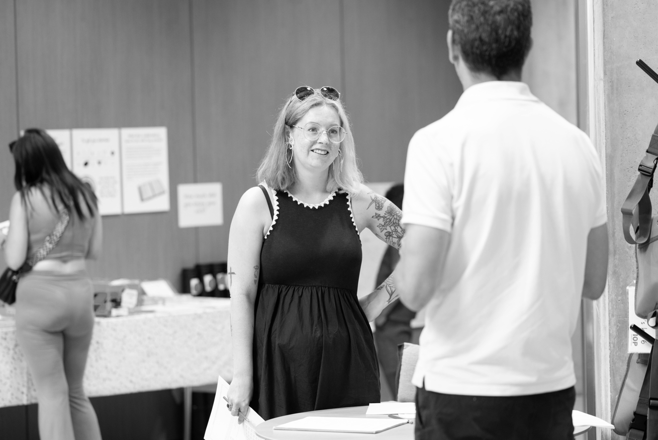 A black and white image of two adult speaking. A woman is facing the camera and a man has his back to the camera