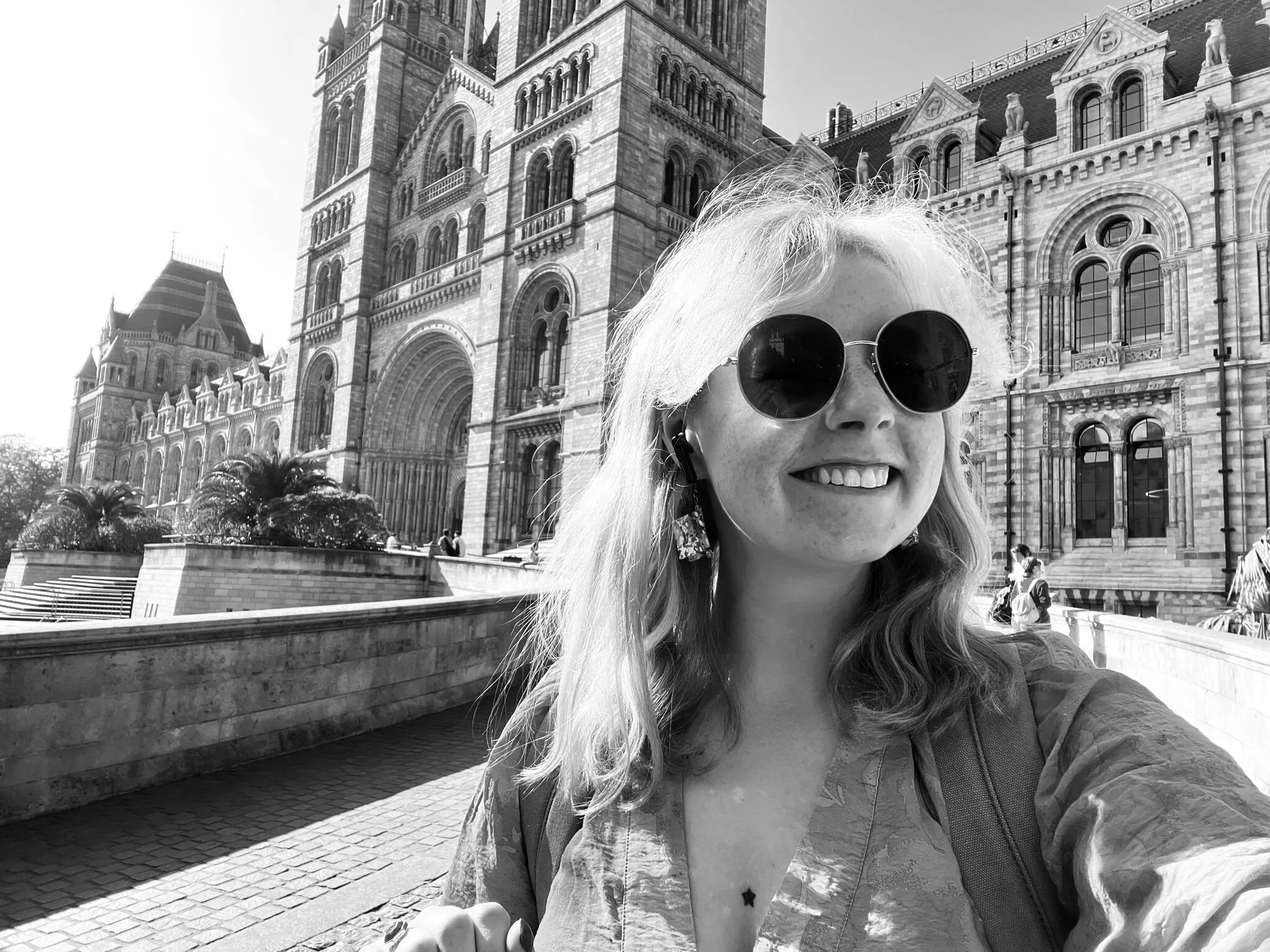 A black and white image of a woman in sunglasses in front of the Natural History Museum