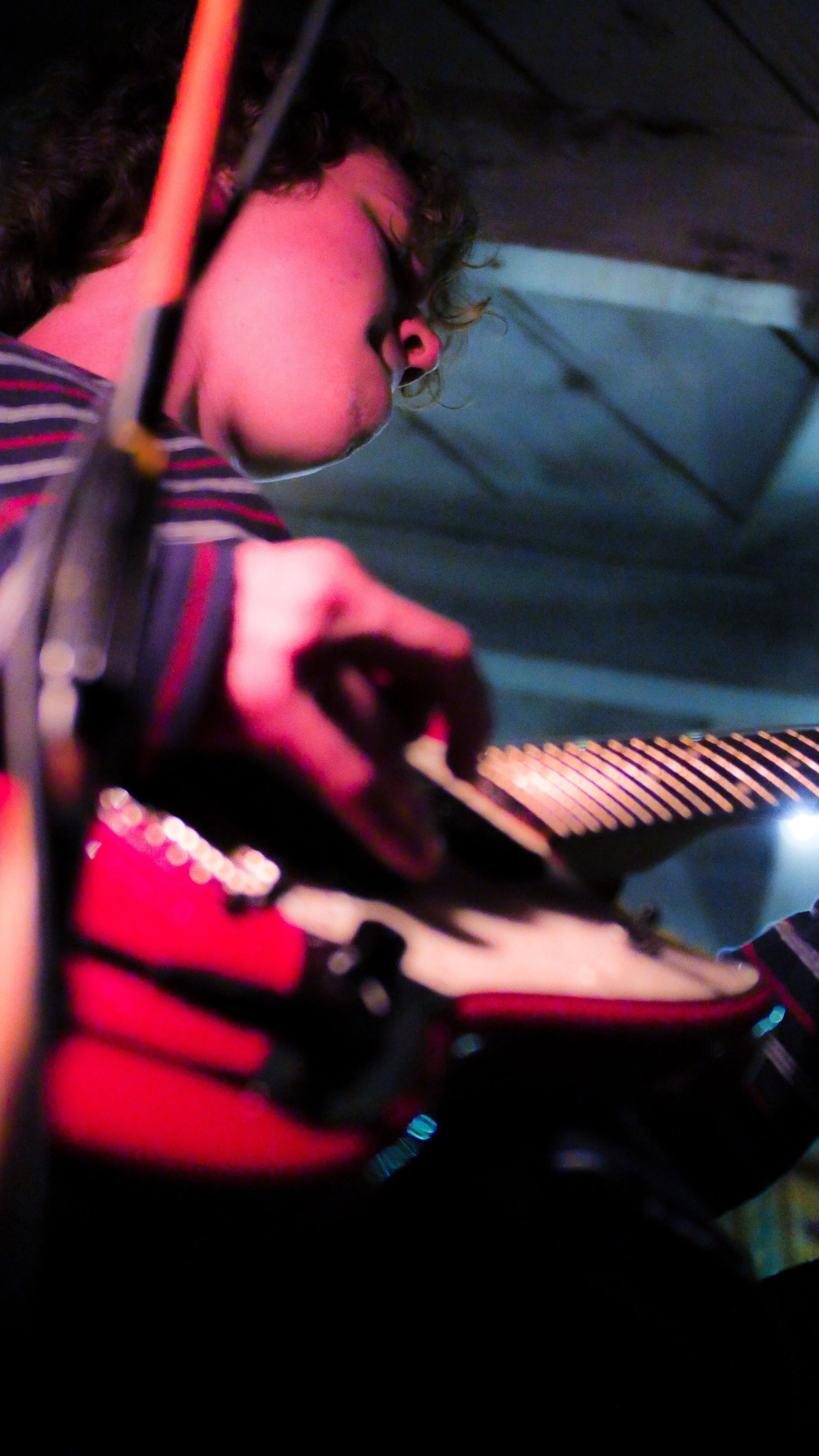 A person with curly hair playing an electric guitar on stage, illuminated by colored stage lights.