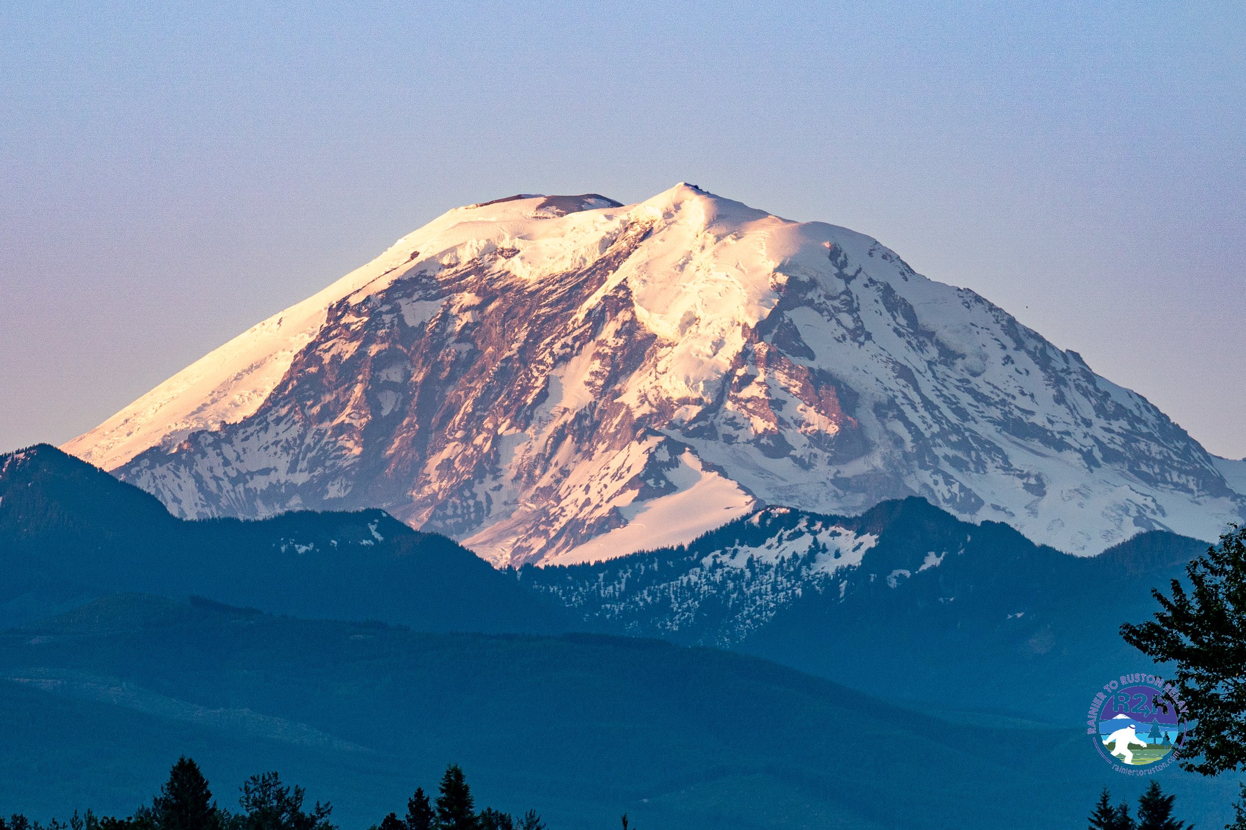 Snow-capped mountain rising above forested hills under clear sky