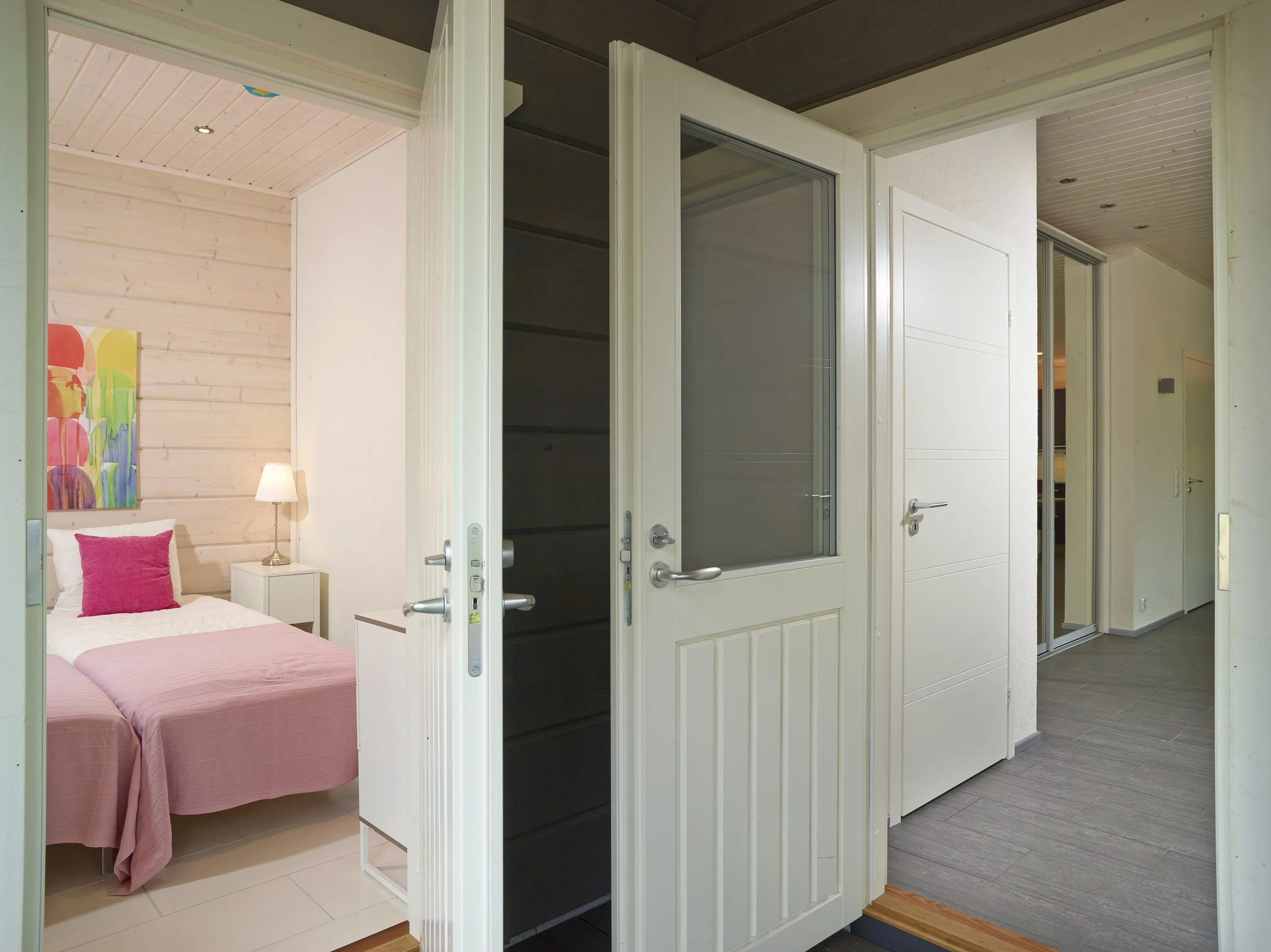 View from a hallway into a bedroom, with open doors and a bed with pink bedding inside the bedroom.