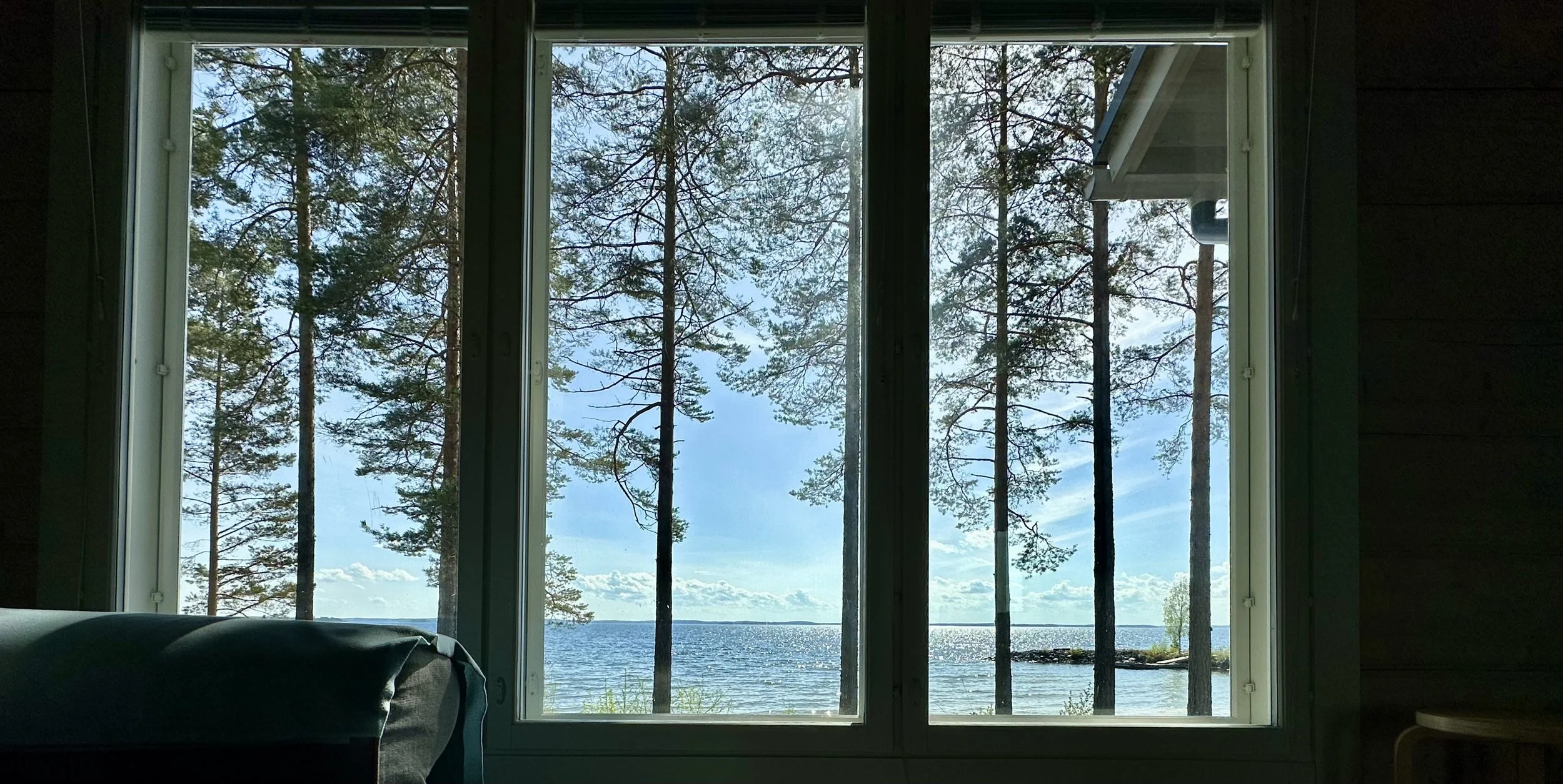 View of pine trees and a lake through a large window in a wooden cabin