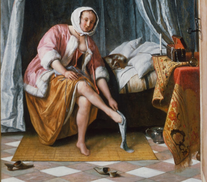 A woman in a pink robe and orange skirt is sitting on a chair, putting on a stocking. She is in a room with a bed in the background and various objects on a table, including a lamp and a decorative cloth. The floor has a checked pattern, and slippers are nearby.