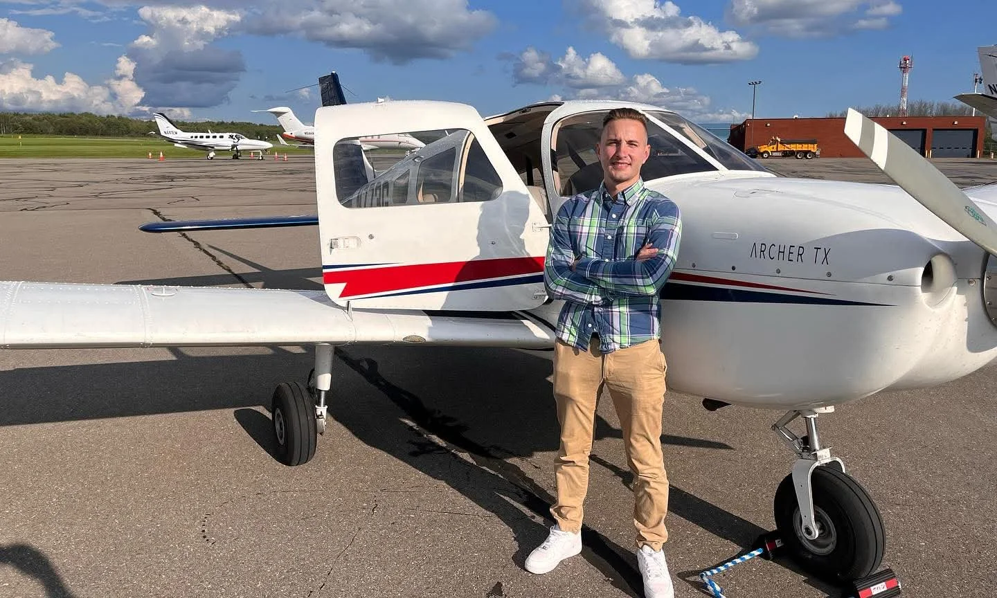 Man standing in front of a small airplane on an airport tarmac.