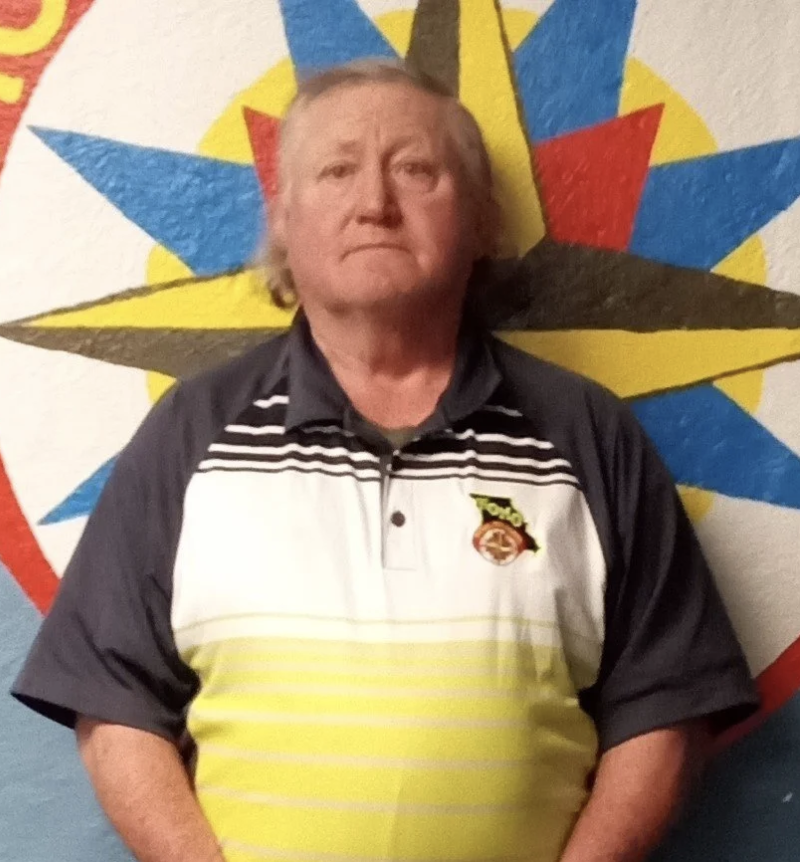 A man with gray hair and a concerned expression standing in front of a Royal Ranger emblem.