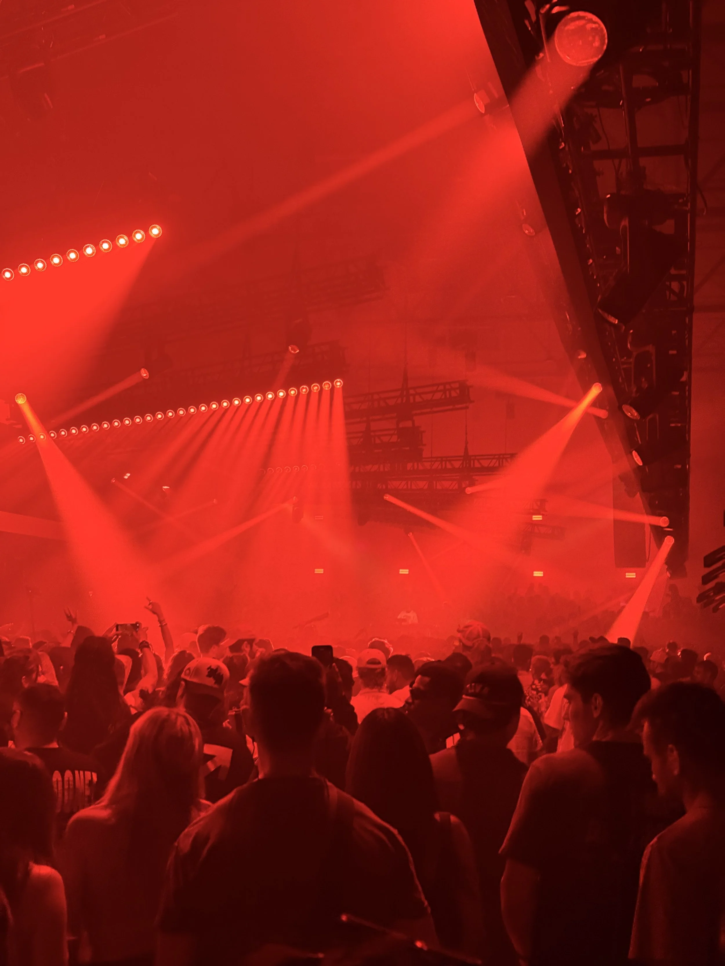 Crowd at a concert or music event with red lighting and stage lights.