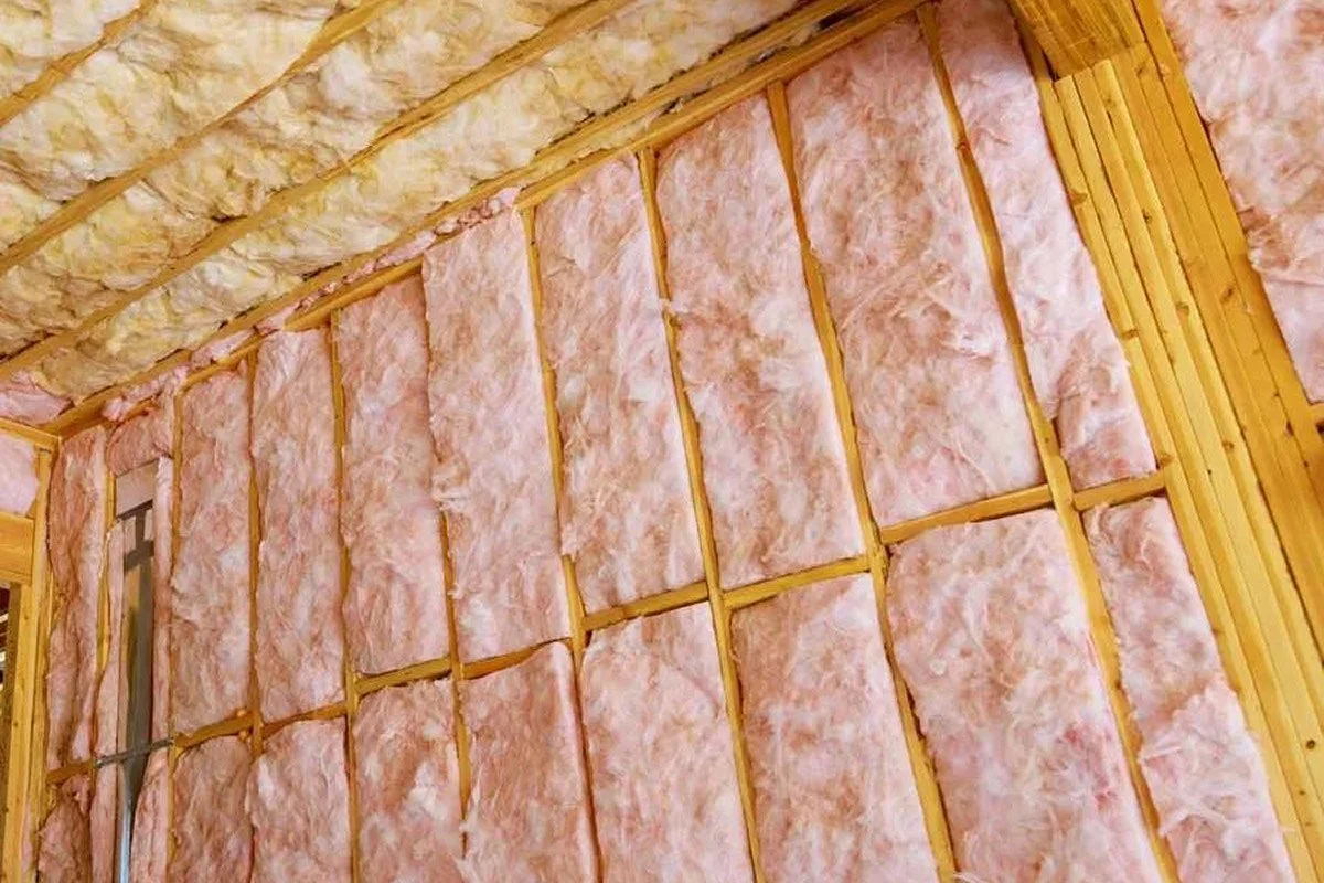 Interior wall with pink insulation batt installed between wooden studs in a building under construction.