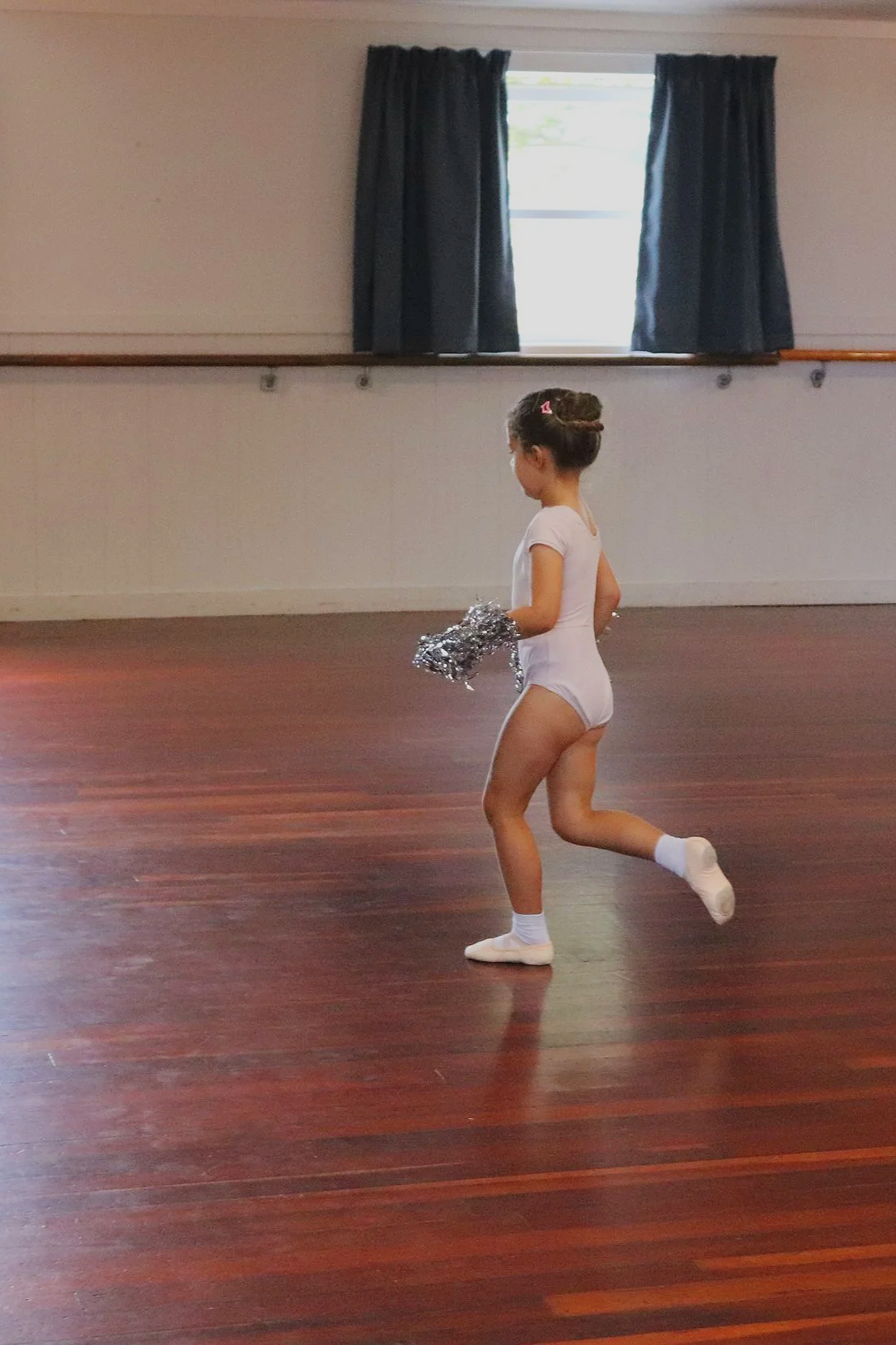 Tiny ballerina runs with silver pom poms in hands
