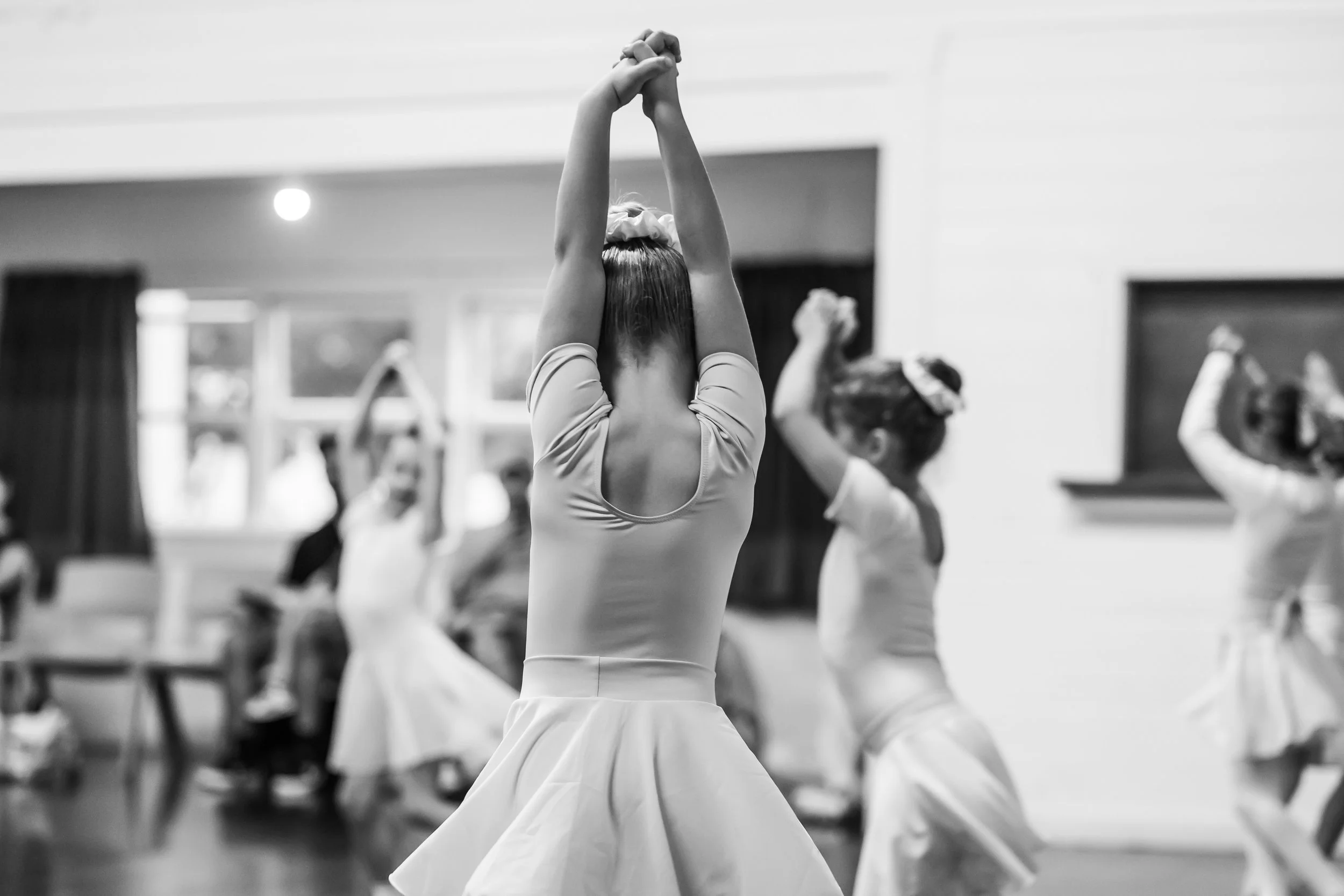 A group of young ballet dancers captured in black and white with their hands in the air