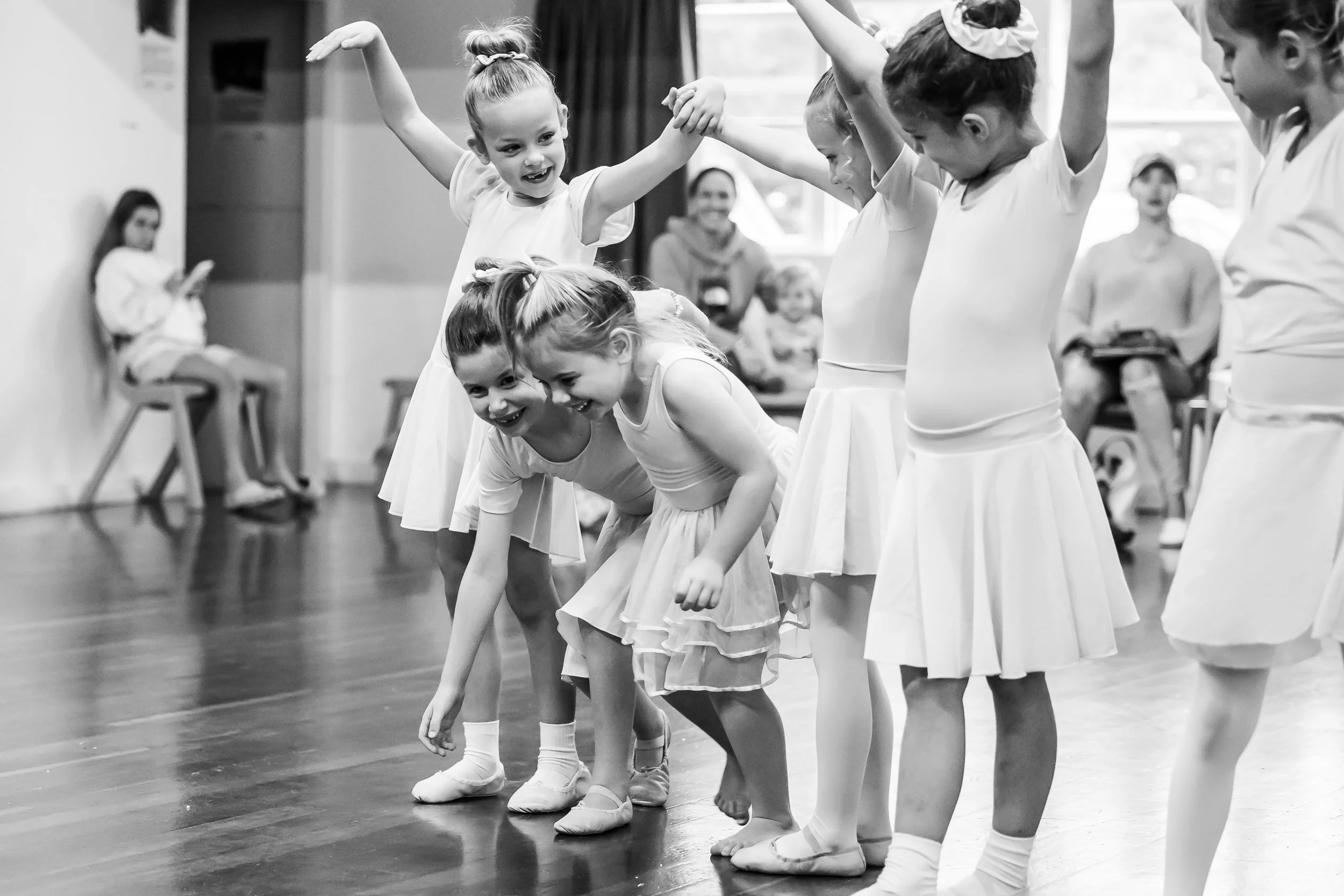 a groups of young dancers standing in a line with two dancers coming through the same window betweem arms of other dancers laughing and having fun
