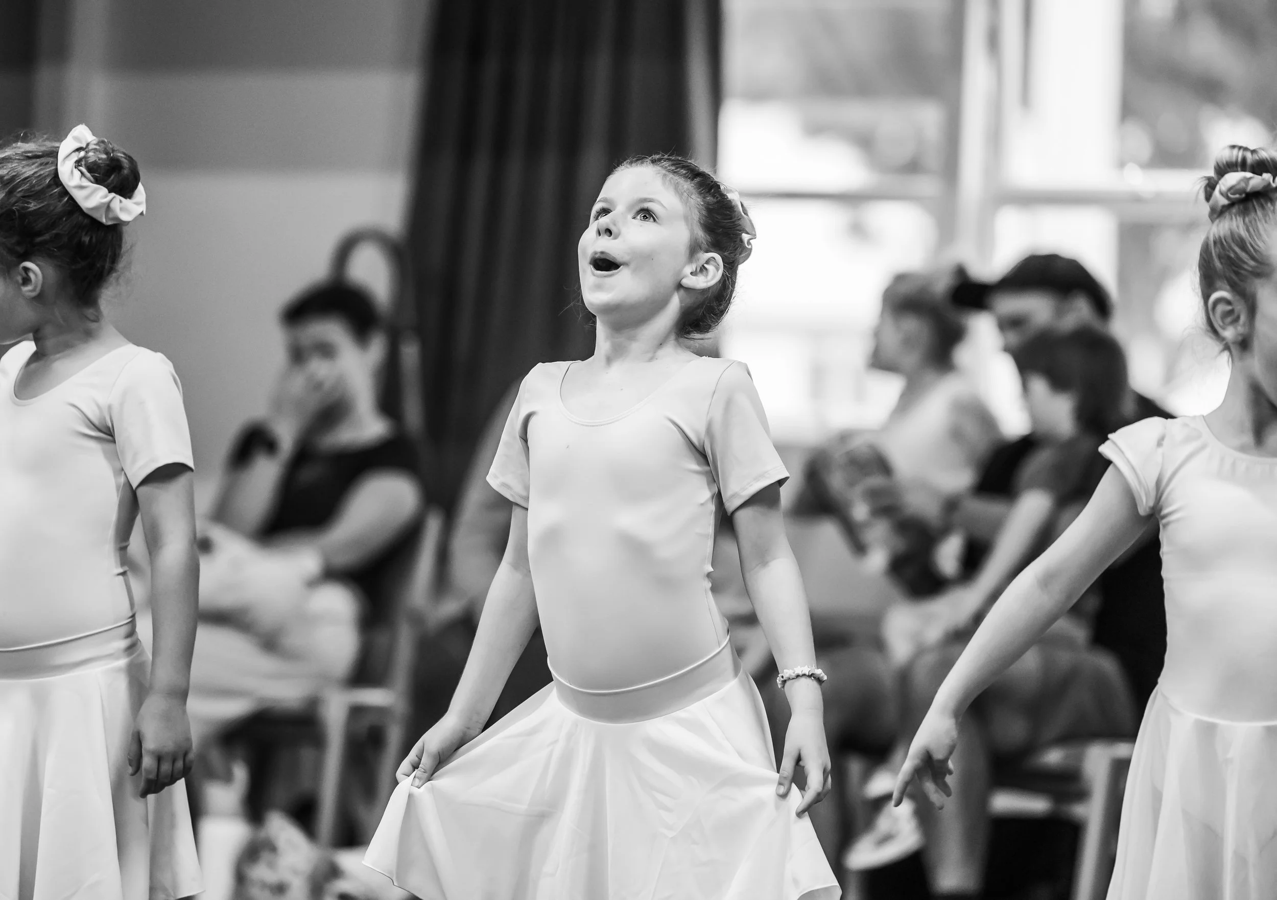 Young ballet dancers captured in black and white photo focused on one dancer with an expressive face showing excitement and awe