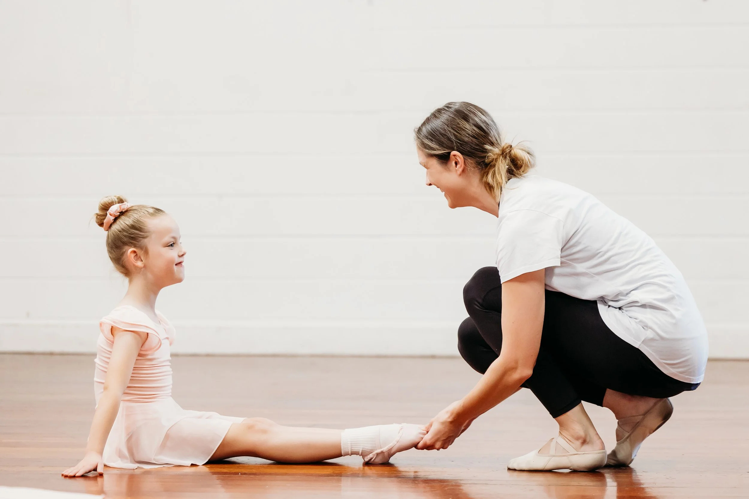 6 year old ballet dancer sitting with legs stretched out in front of them and teacher Jessica Opacic holding feet in pointed position