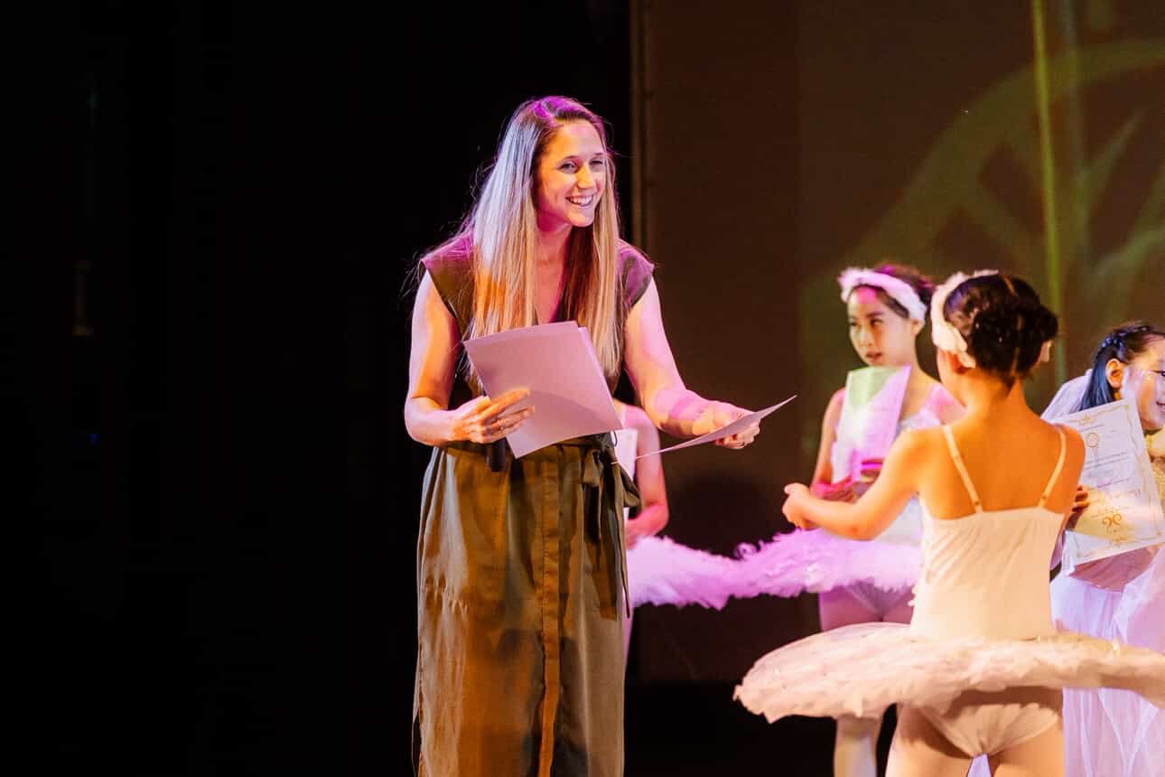 Ballet instructor smiling while talking to young ballet students on stage