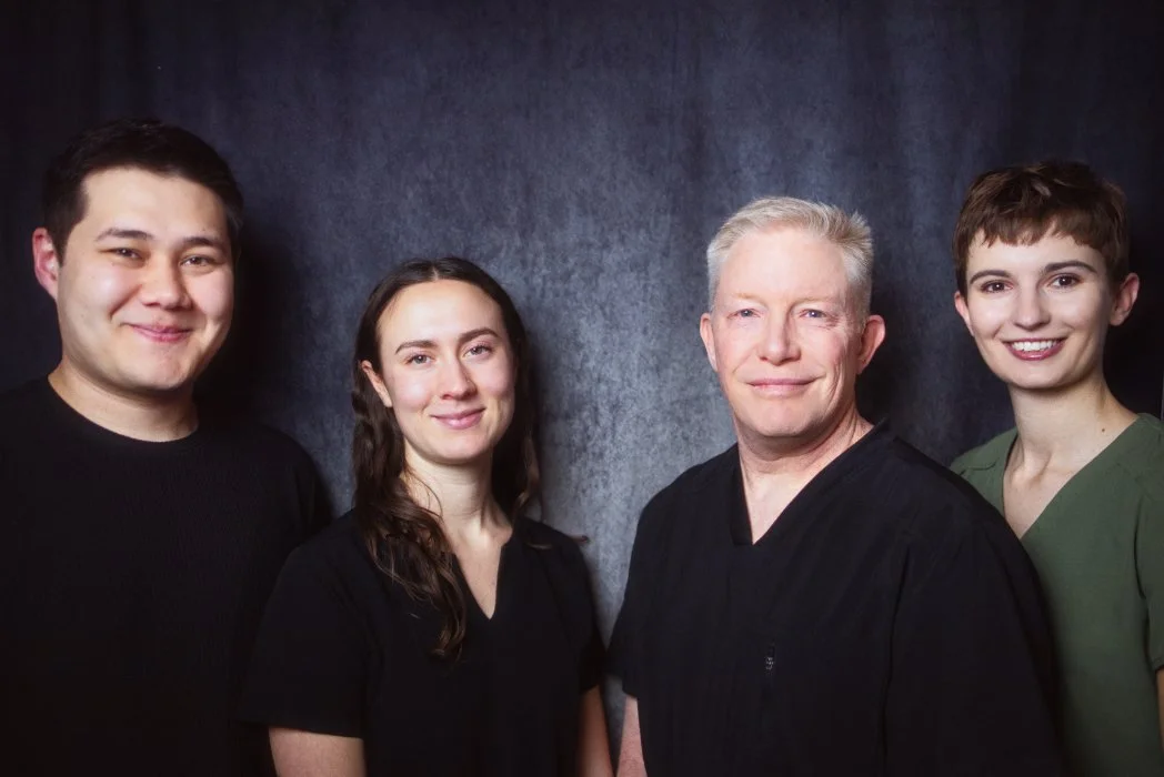Team portrait of four people, including a man and woman in medical scrubs, against a dark background.