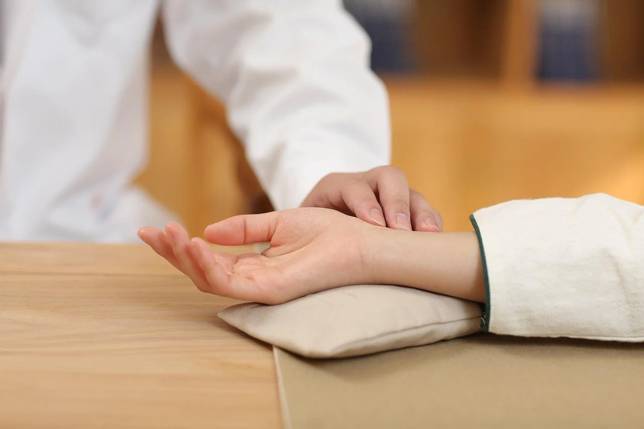Person receiving a wrist massage at a wooden table, with the person providing massage using their hands.