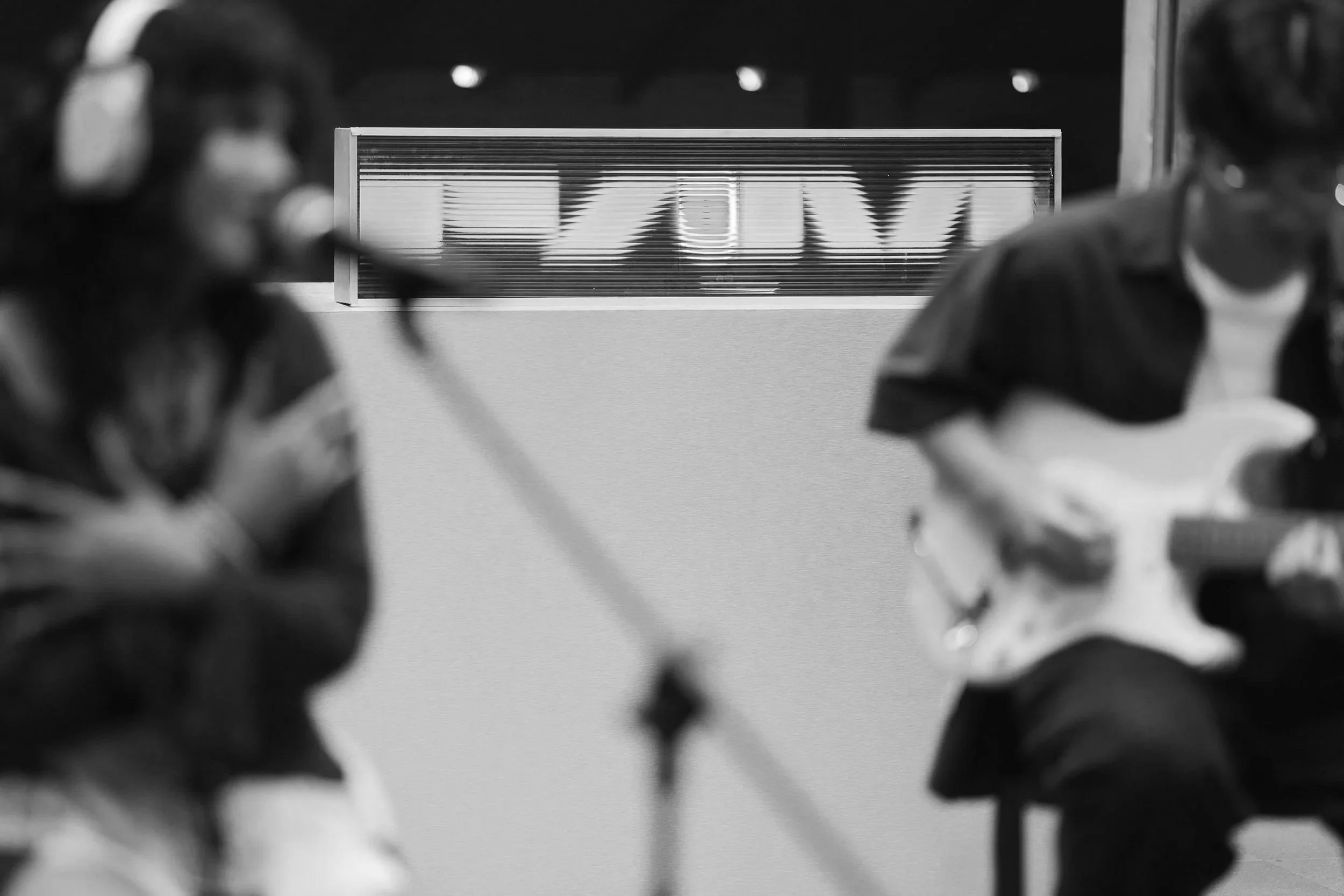 Black and white photo of two musicians, including Bangkok-based flower.far, one playing a guitar and the other singing into a microphone, with a blurred FAM (88rising's Future Asian Music) sign in the background. Taken at FAM Studios with Cloud11.