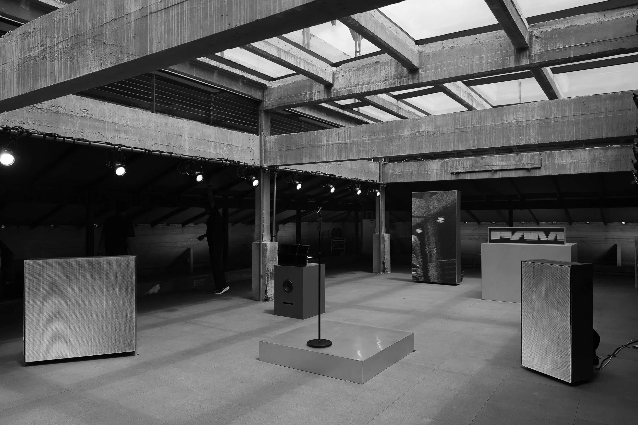 FAM Studios Bangkok event space with a small stage, a microphone, and various displays, under an industrial concrete structure with a glass ceiling.