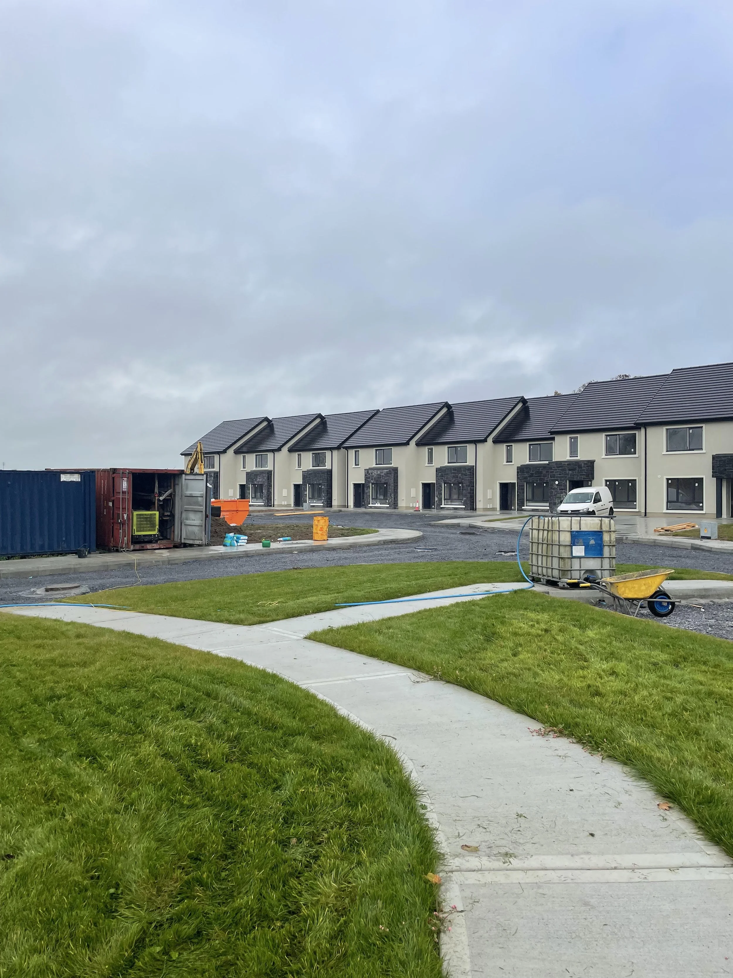 Construction site with newly built townhouses, construction materials, and equipment on a cloudy day.