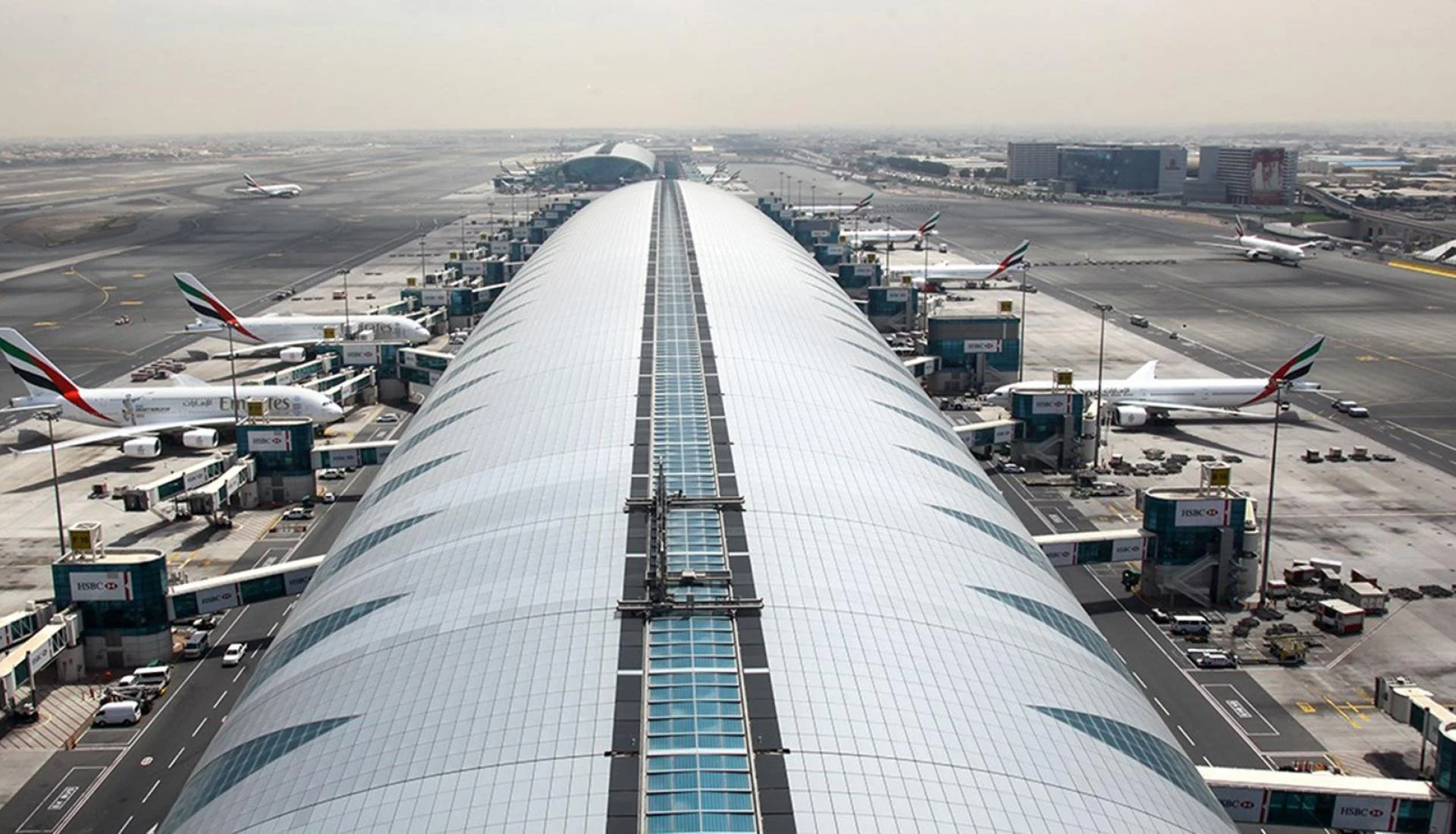 View of Dubai International Airport terminal with multiple Qatar Airways aircraft parked at gates and connected to the terminal through jet bridges.
