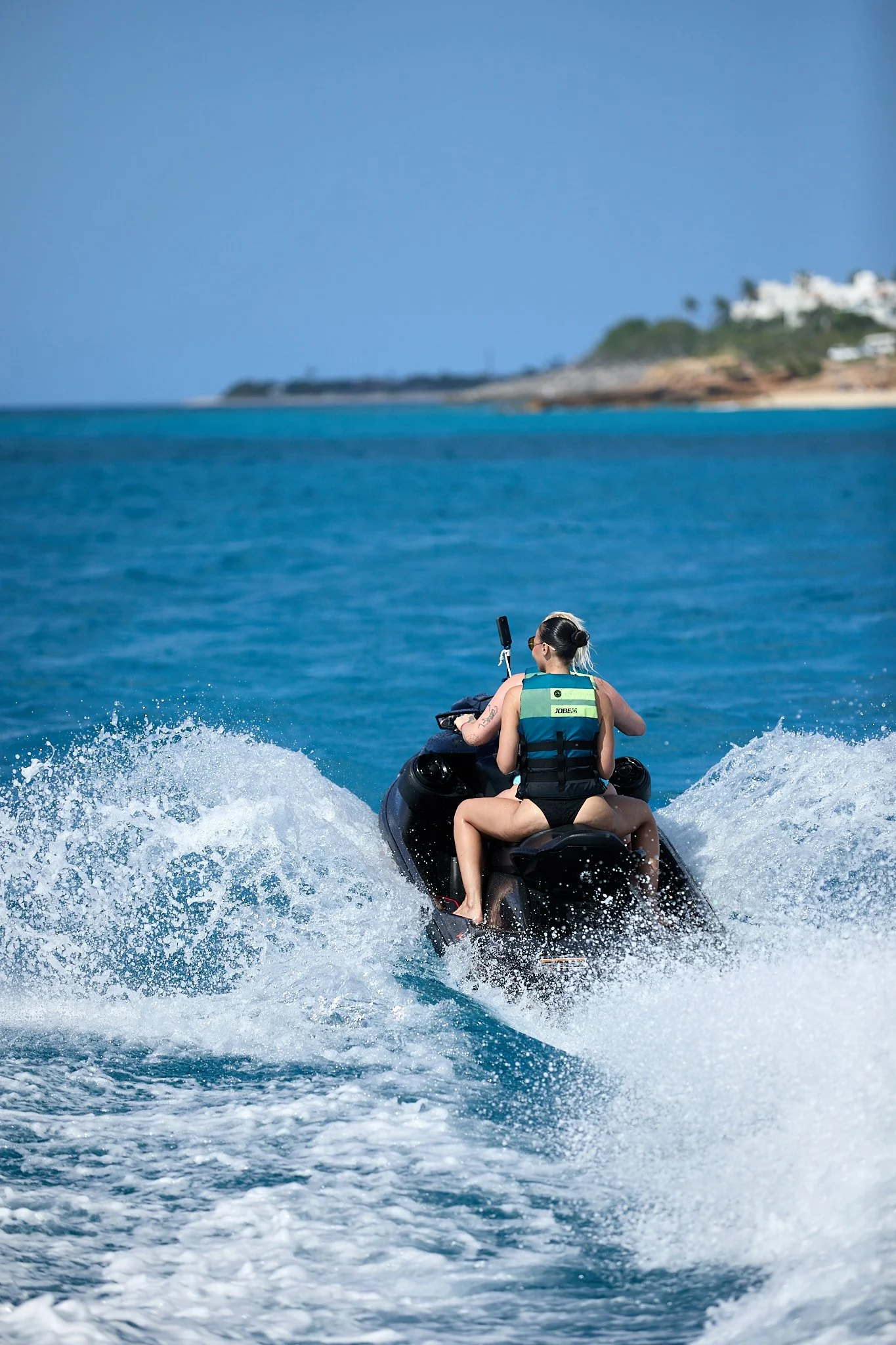 A person riding a jet ski on the ocean with a clear blue sky and distant shoreline in the background.