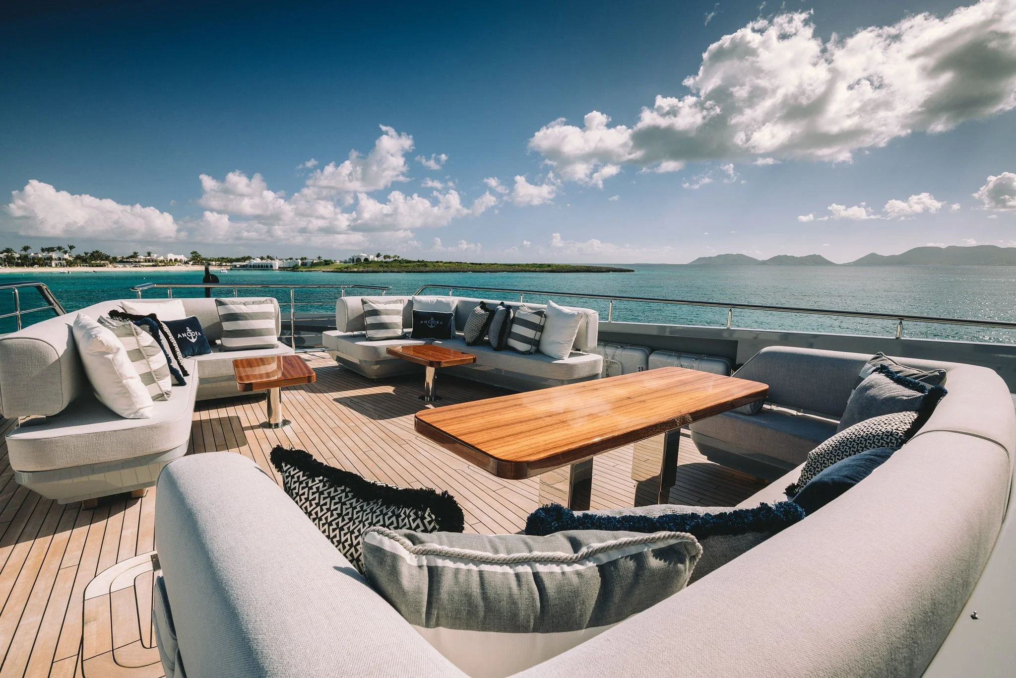 Luxury yacht deck with outdoor seating and wooden tables overlooking the ocean under a partly cloudy sky.