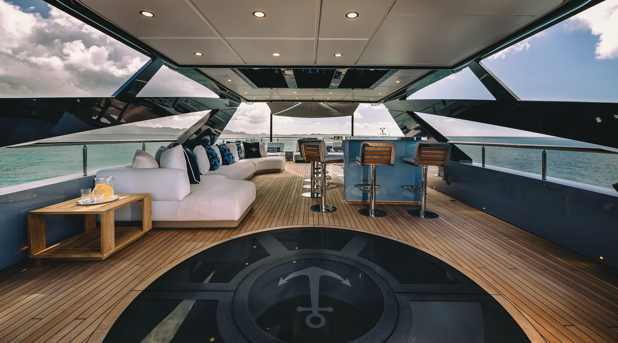 View of a luxury yacht covered deck with a seating area, bar stools, and an ocean view.