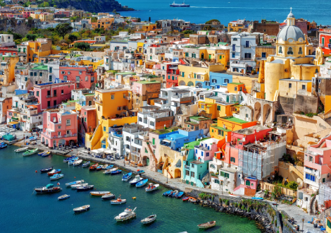 vibrant and colorful buildings follow the coastline, where many colorful boats are harbored.