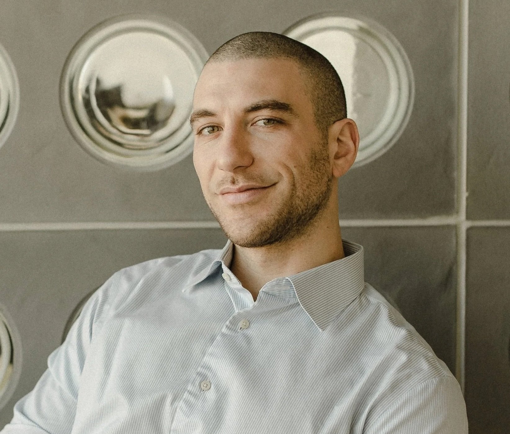 Headshot of man with shave head and close cut facial hair in blue dress shirt.