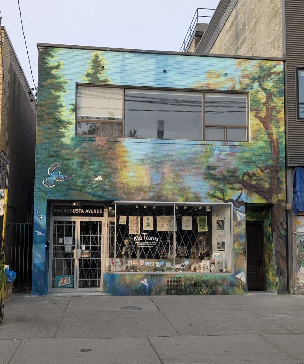 Facade of a storefront with a colorful mural featuring trees, birds, and nature scenes.