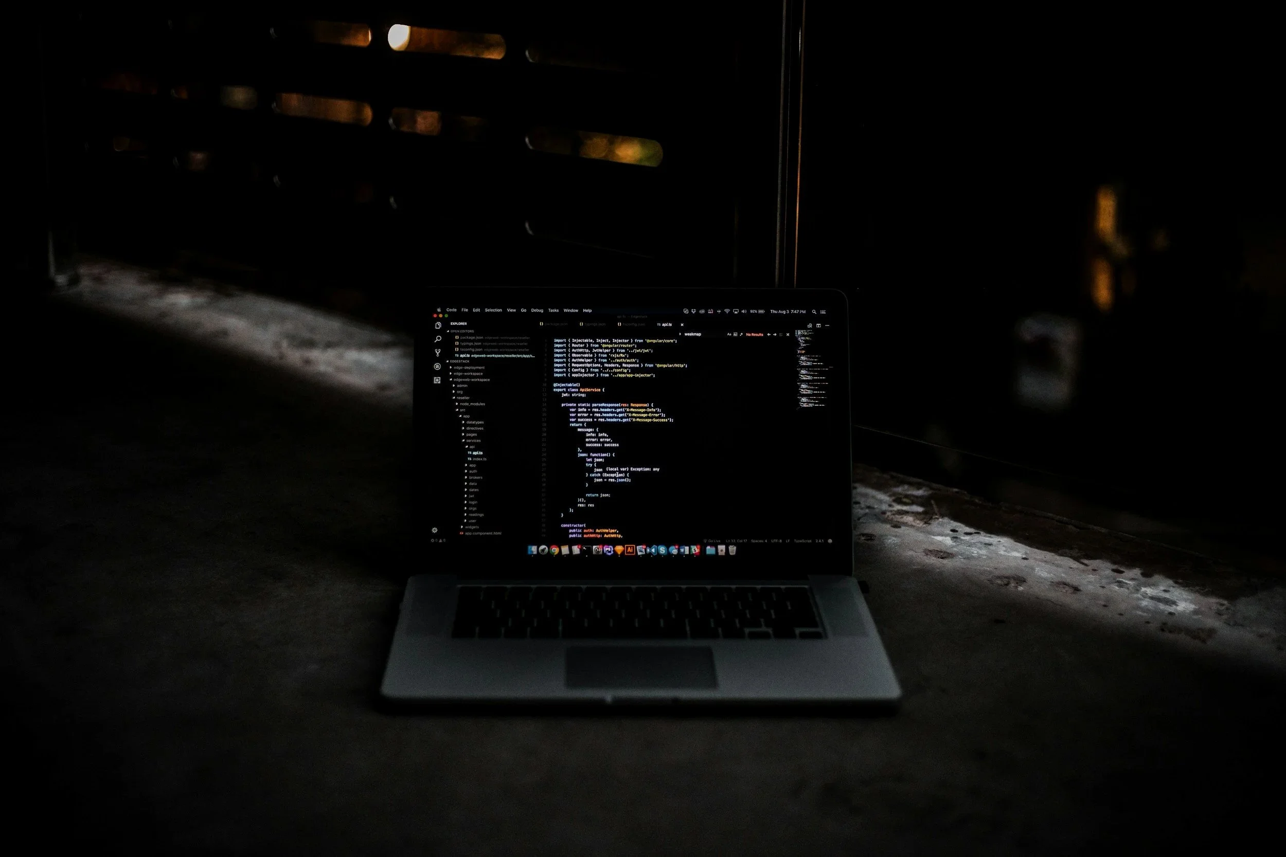 A laptop displaying code on its screen placed on the ground in a dark environment with minimal lighting coming from the left side.