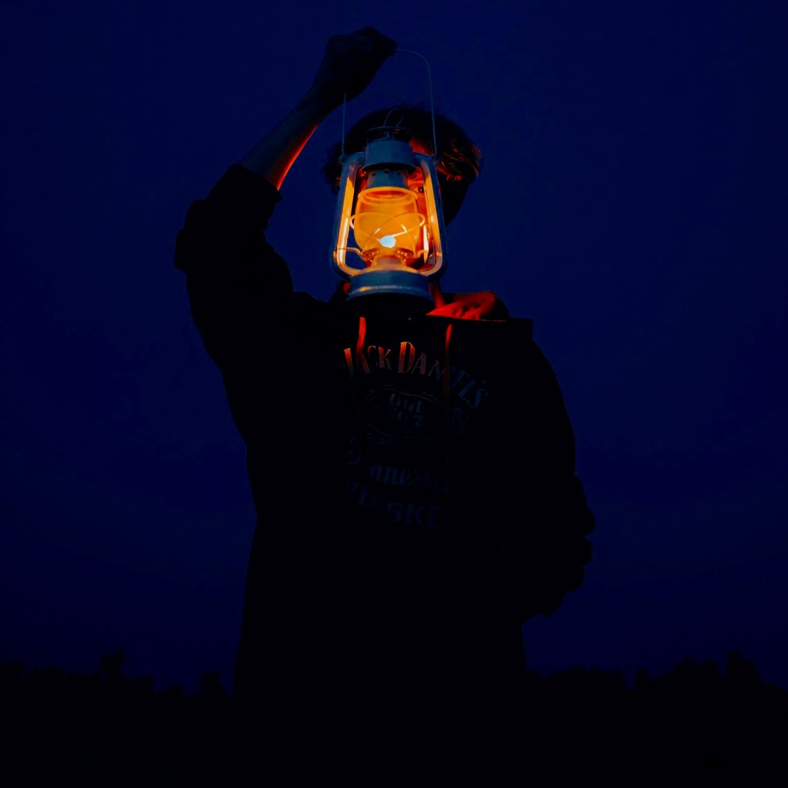 Person holding an orange lantern against a dark evening sky