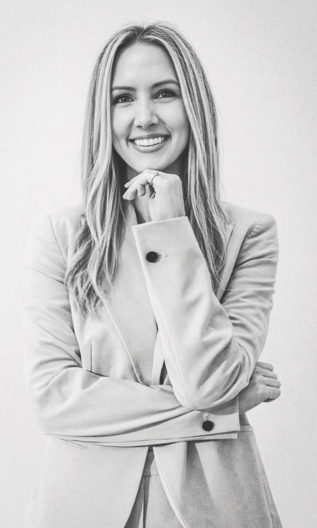 Black and white portrait of a smiling woman with long hair, wearing a blazer, with her right hand resting on her chin.