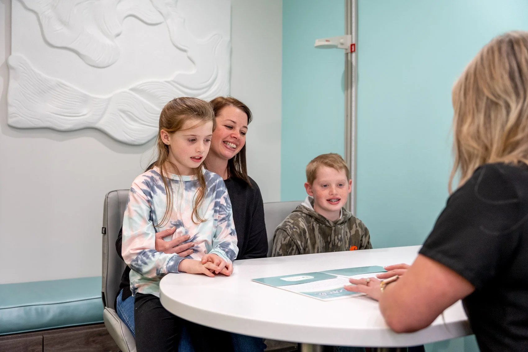A mother and her two children review treatment details with a Weiler Orthodontics team member during a consultation