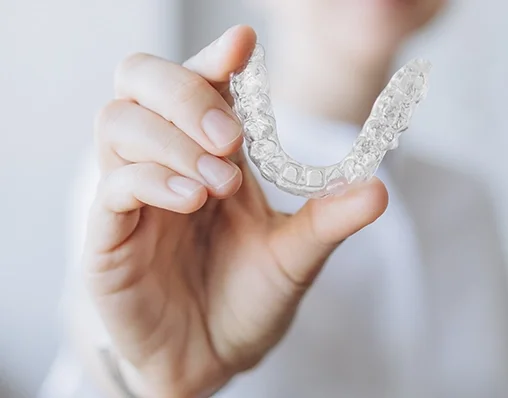 Person holding a clear dental retainer in their hand.
