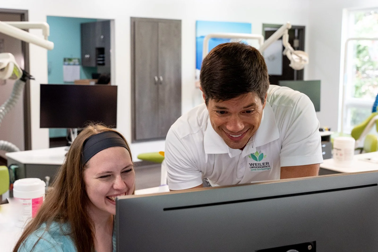 A man and woman in a dental office looking at a computer monitor and smiling.