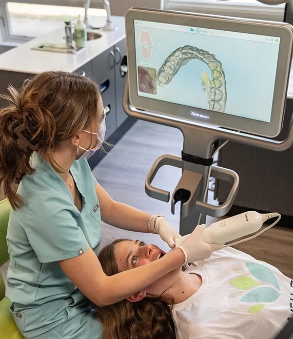 Dental professional using digital scanner on patient with 3D dental imaging on monitor in a dental office.