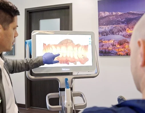 Dental professional pointing at a digital dental impression on a screen in a dental clinic.
