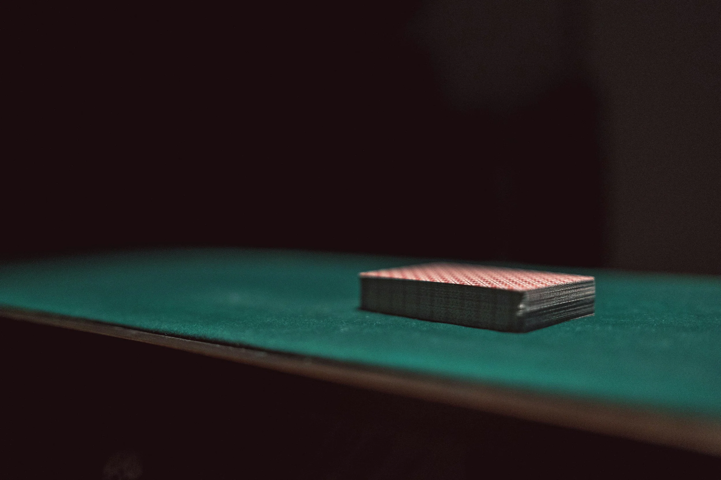 A deck of stacked playing cards on a green felt surface, with a dark background.