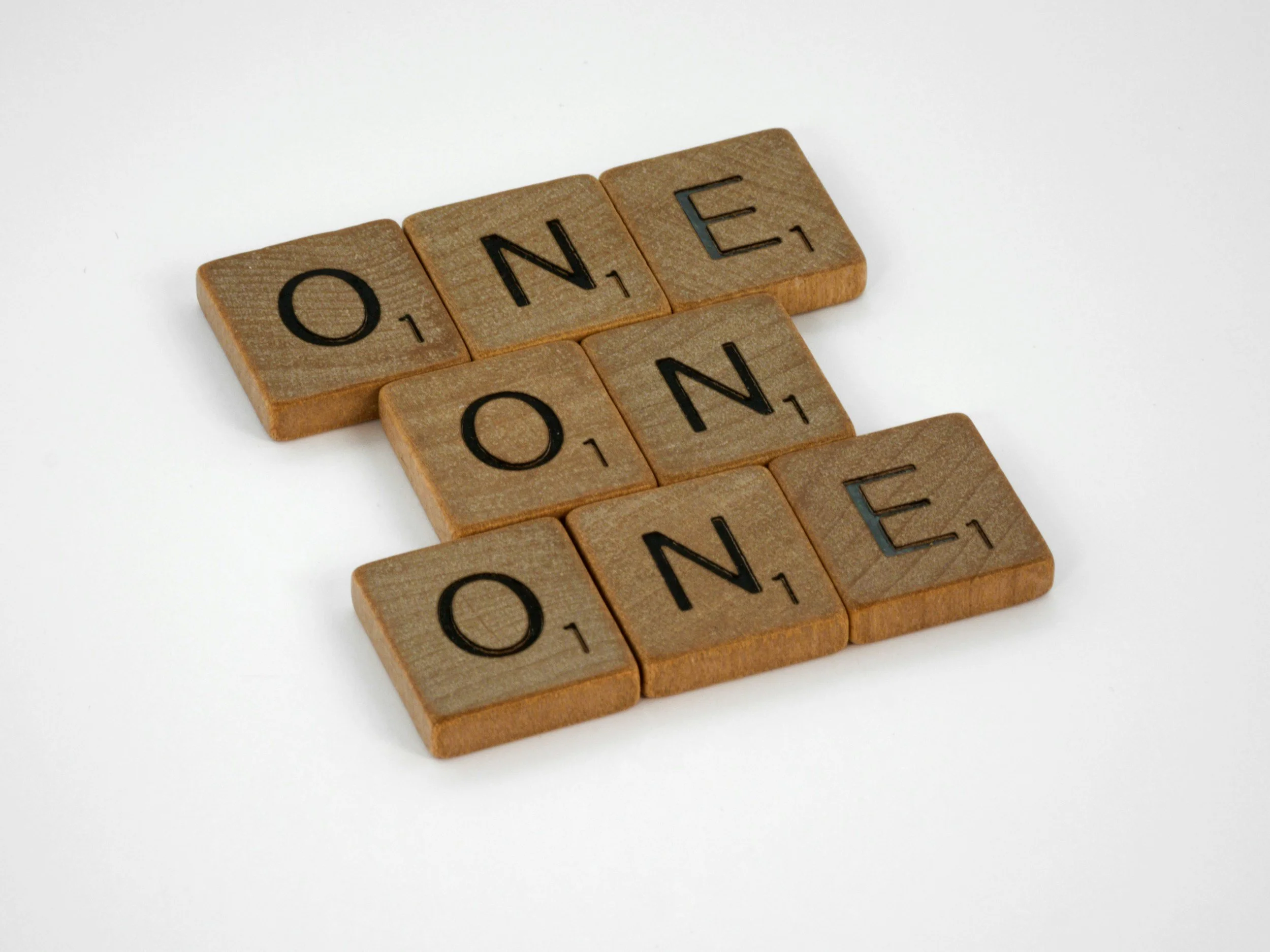 Scrabble tiles spelling the word 'ONE' arranged on a white surface.