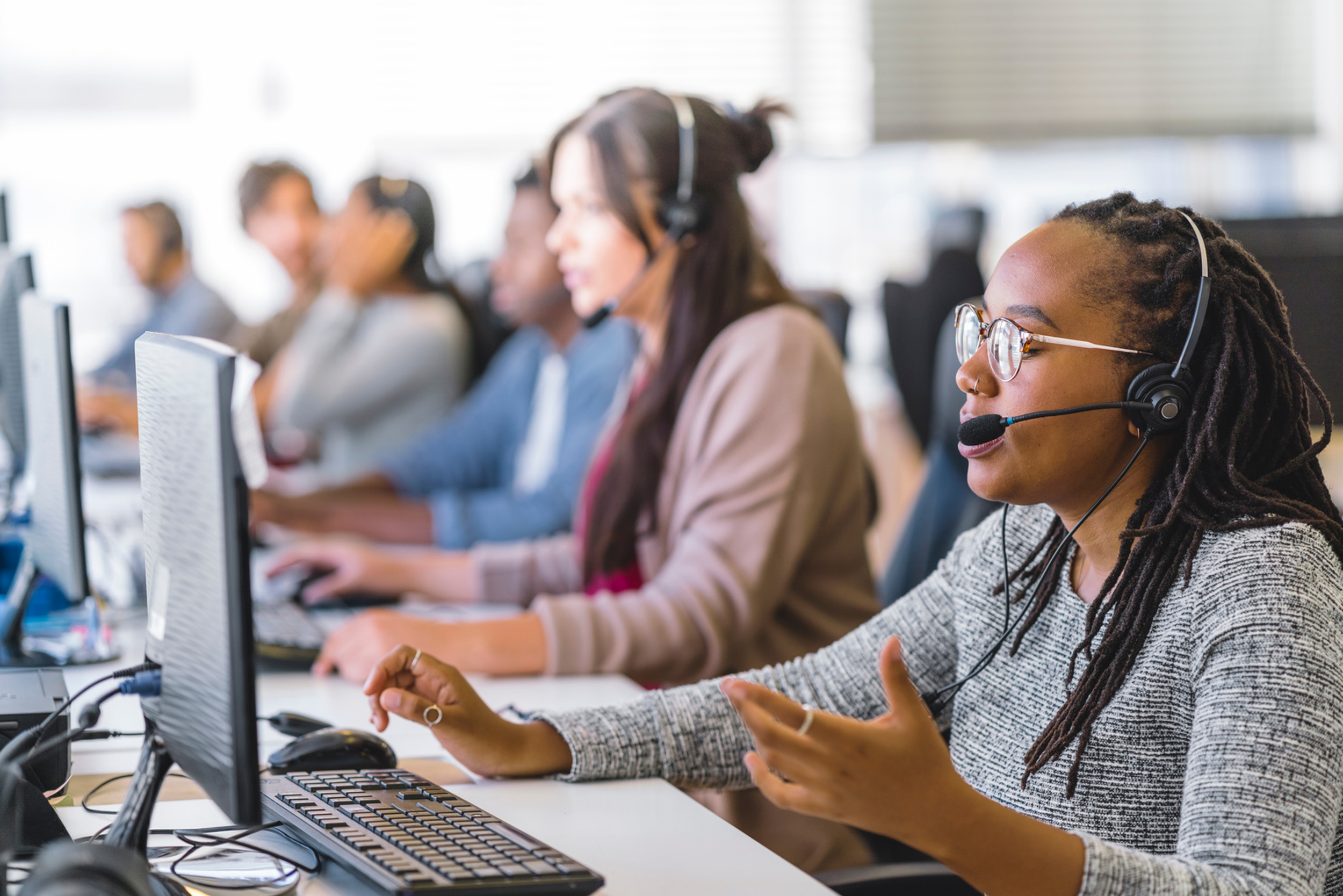 Support agents working at a call center, wearing headsets and using computers in an office setting.
