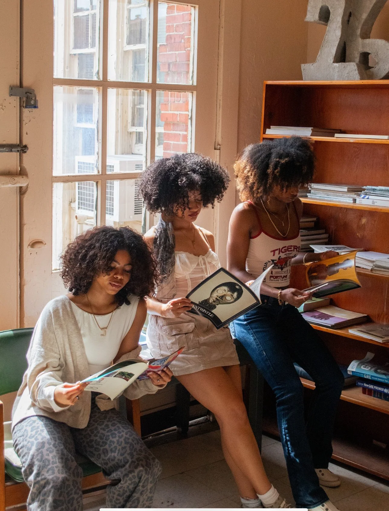 Three women sitting in a room and reading magazines or brochures.