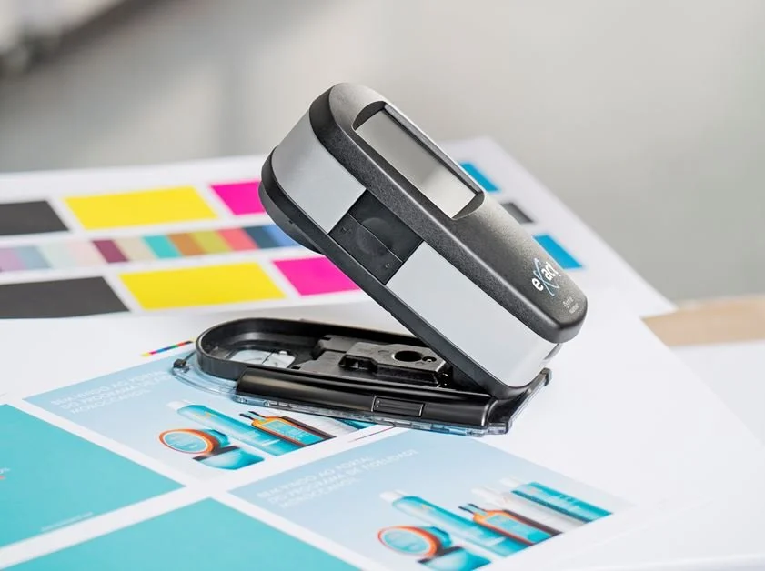 Handheld spectrophotometer scanning CMYK color chart on printed materials for GMI certification and accuracy